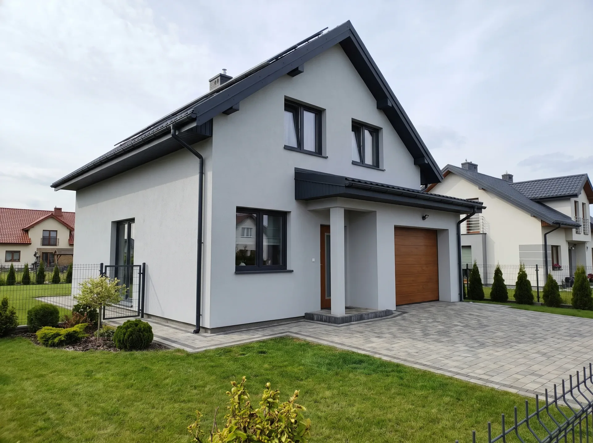 Biała elewacja nowoczesnego domu z czarnym dachem i brukowanym patio